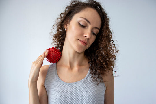 Woman performing myofascial release on the neck muscle with a red spiked ball. Concept: practice self-care with props at home, self-massage.