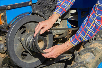 belt replacement on a tractor,the man's hands put a belt on the motor pulley of the walk-behind tractor - obrazy, fototapety, plakaty