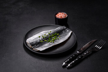 Marinated fillet with spices and herbs of sea herring on a black plate