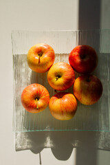 A set of apples on a transparent dish. Apples are yellow-red. Hard light.
