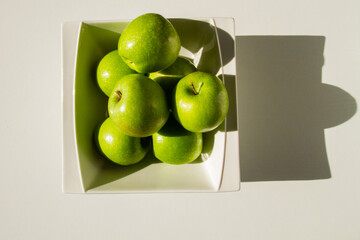 A set of green apples in a bowl. Green apples. Hard light. Shadow.
