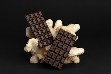Two large chocolate bars on a coral on black background.