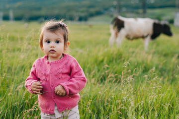 Caucasian baby girl standing on grassy field looking curiously at the camera. Copy space. Kid exploring nature.