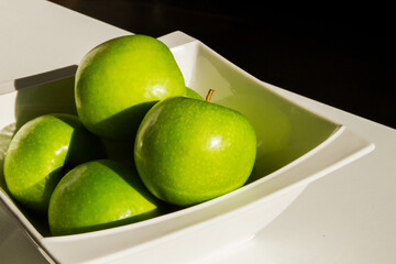 A set of green apples in a bowl. Close-up. Green apples. Hard light. Shadow.