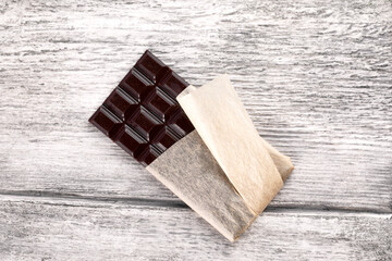 Top view of dark chocolate bar in craft package on gray wooden background