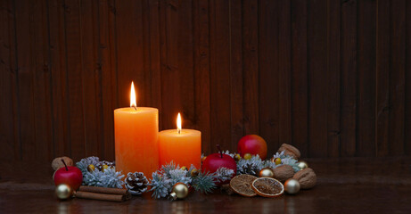 Rustikale Weihnachtsdekoration vor einer Holzwand mit brennenden Kerzen ,Zweigen, Zimtstangen und Nüßen.