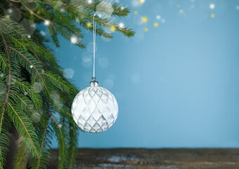 A white Christmas ball hangs on a fir branch. Christmas decoration on a blue background with blurry lights, highlights and copy space. High quality photo