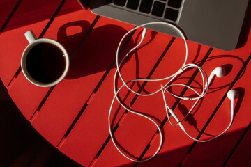 Cup with coffee and a laptop and headphones on a red table. Kind of light. Hard light, shadows, top view.