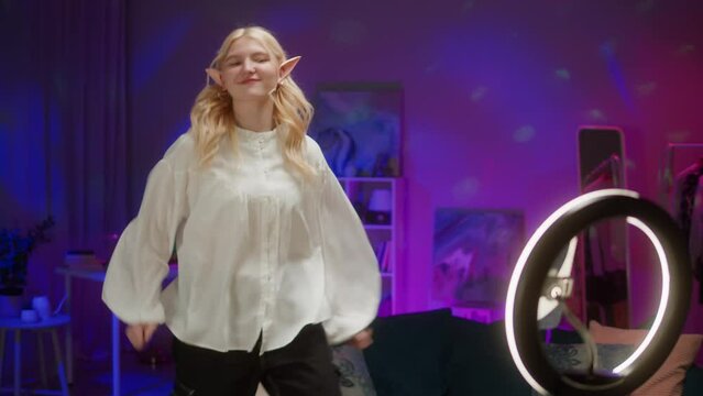 Woman recording dance video in living room. Teenager elf dancing at home for musical clip. Blogger making music content for channel, wearing elves ears.