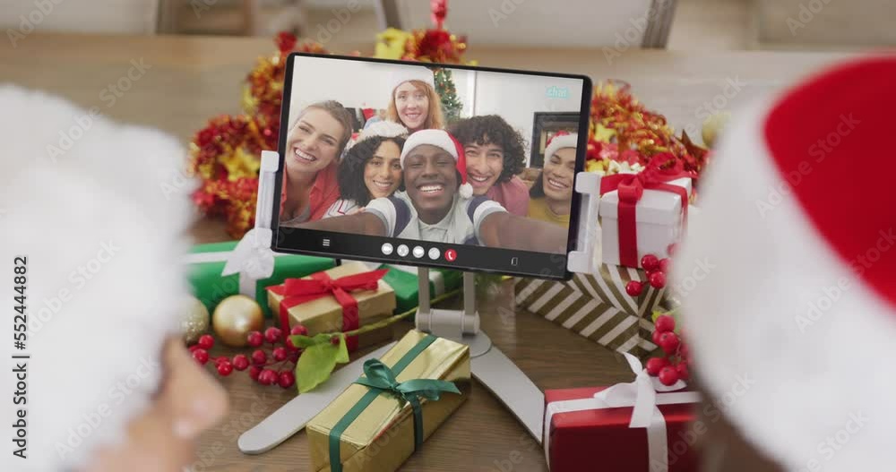 Wall mural Caucasian couple with santa hats having tablet video call with happy diverse friends