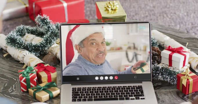 Diverse friends with santa hats having laptop video call with happy biracial man