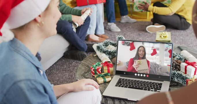 Diverse friends with santa hats having laptop video call with happy biracial woman