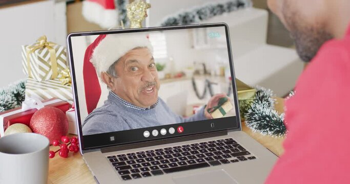 African american man with santa hat having laptop video call with happy biracial man