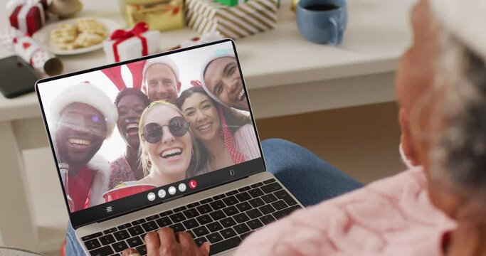 African american woman with santa hat having laptop video call with happy diverse friends