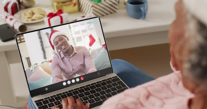 Animation of african american woman in santa hat on laptop video call with man at christmas