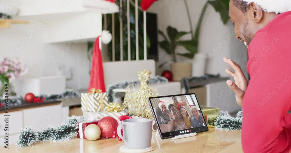 Canvas Prints Animation of african american man in santa hat on tablet video call with friends at christmas