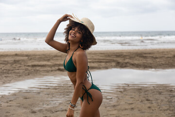 Fototapeta na wymiar Portrait of beautiful afro girl smiling with hat and bikini with beach background.
