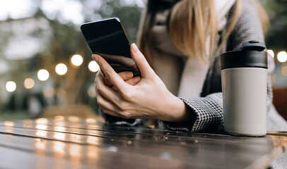 Girl holding phone with coffee in cafe on street with lights close-up