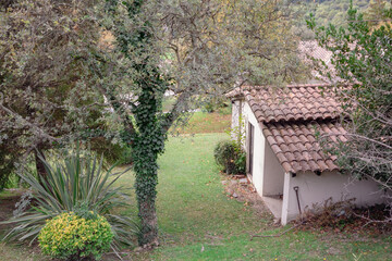 Peque&ntilde;a casa del pueblo catal&aacute;n en medio del monte con un precioso jard&iacute;n verde con &aacute;rboles con enredaderas que lo rodean.