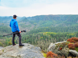 Photographer with folded tripod on end of cliff thinking. NAtural forestry landscape