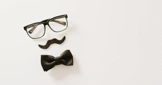 Video of black false moustache, glasses and bow tie on white background with copy space