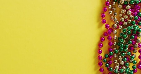 Video of pink, gold and green mardi gras carnival beads on yellow background with copy space - Powered by Adobe