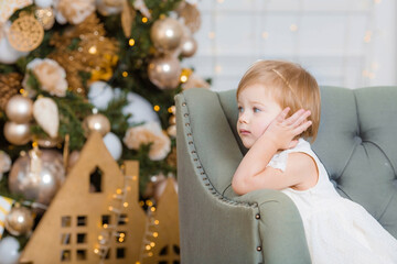 Merry christmas and happy New year! Portrait of a beautiful little one-year-old girl on the sofa in the living room. The concept of children's recreation, family and holiday.