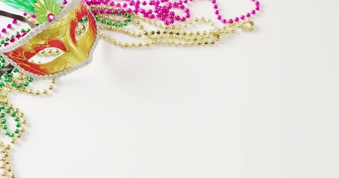 Video of gold masquerade mask and mardi gras beads on white background with copy space