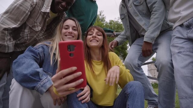 Group of students outside looking at a mobile phone. A cheerful girl tells her friends to take a selfie. University classmates connected by social networks.