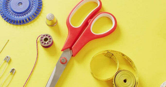 Video of tape measures, needles, pins, scissors, thimble and sewing threads on yellow background