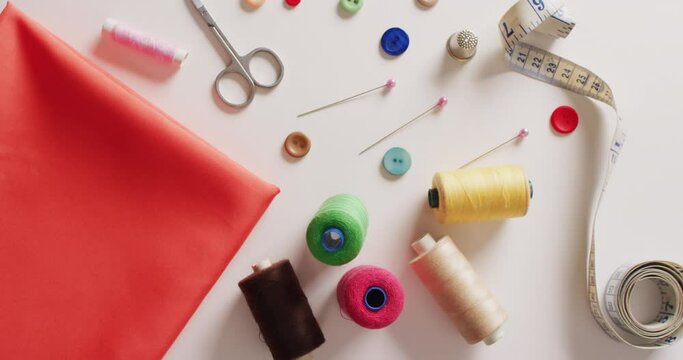 Video of fabric with tape measure, scissors, buttons, pins and cotton reels on white background