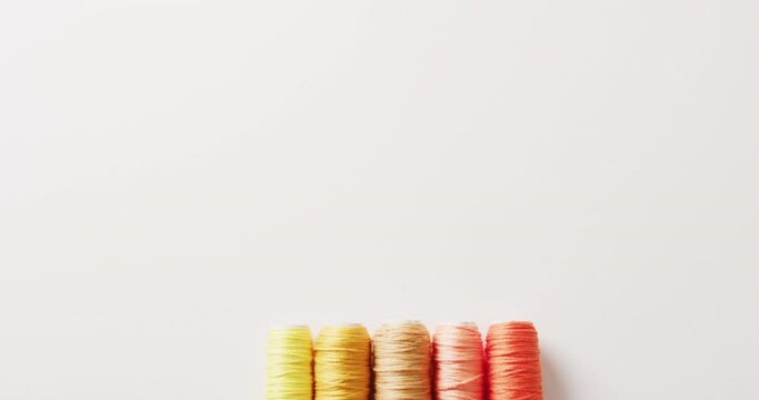 Video of five reels of yellow to orange embroidery threads on white background with copy space