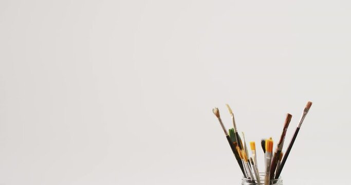 Video of a collection of paintbrushes standing in a jar on white background with copy space