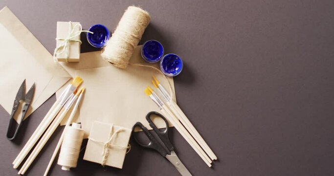 Video of parcels with twine, card, scissors, brushes and paint on grey background with copy space