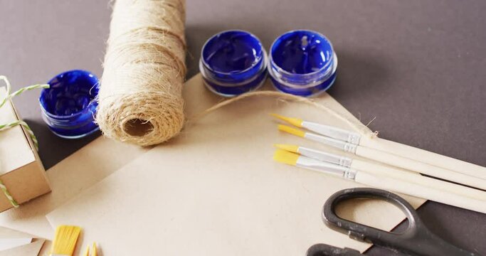 Video of parcel with twine, card, scissors, brushes and paint on grey background