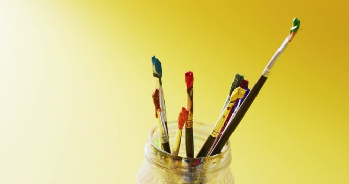 Video of a collection of used paintbrushes standing in a jar on yellow background with copy space