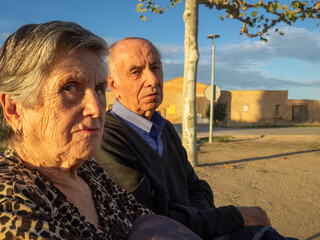 Elderly couple sitting on bench with angry and stern look.