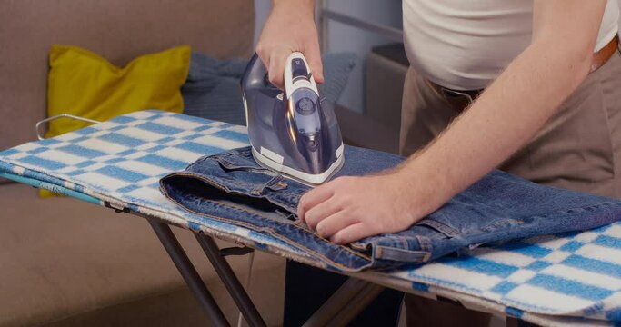 Man ironing jeansliving in bright room domestic daily life. Household man