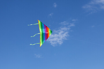 Flying kite. Rainbow kite hovers in the air high in the sky. Blue sky with clouds