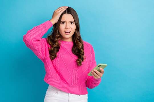Photo of young funny stressed teen girl wear pink pullover touch head oops mistake hold phone hacked problems isolated on blue color background