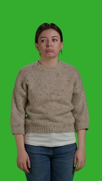 Vertical video: Front view of discontent mad girl acting upset and displeased, posing over green screen background, being disappointed and discouraged. Sad female model standing over full body studio