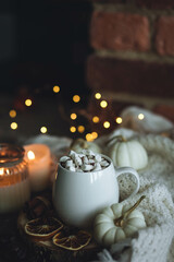 Autumn cozy home composition with hot chocolate with marshmallow and candles. Aromatherapy on a grey fall morning, atmosphere of cosiness and relax. Wooden background, window sill, close up.