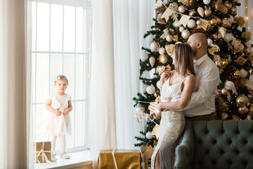 Merry Christmas! Mom, dad and little daughter dressed up at a beautiful Christmas tree in the living room. Family morning on Christmas eve, waiting for gifts. The concept of family unity.