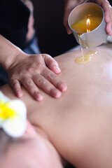A candle massage and hand of therapist hold a burning candle pot contain essential oil pouring on a...