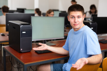 Young male student turned around and looking at camera during lesson in college computer class, throwing up hands