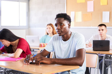 African American student attending teacher lesson at classroom. Black guy in class study with a multiracial high school college. Young boys and girls sitting at desk. Education concept. High quality - Powered by Adobe