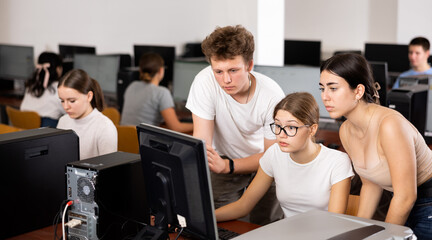 Fototapeta premium Concentrated boy helping young female students working with pc in library computer class