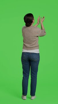 Vertical video: Back view of optimistic girl saying congratulations and applauding on camera, doing standing ovation gesture and clapping hands. Smiling female model celebrating success, greenscreen