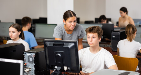 Female teacher helping teenage boy with task solution during lesson in computer class.