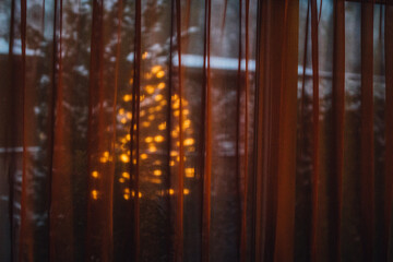 reflection of christmas tree lights through golden curtain and snowy outdoors